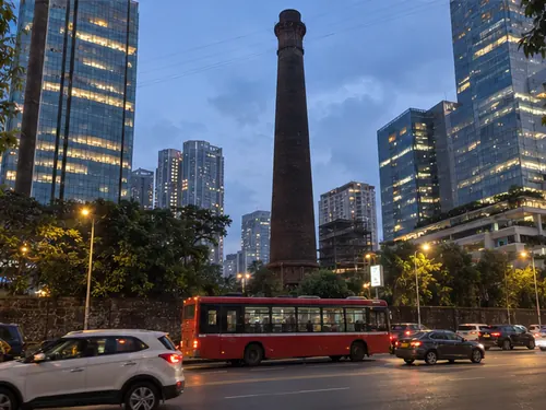 An old mill chimney between new glass office towers in Lower Parel at dusk